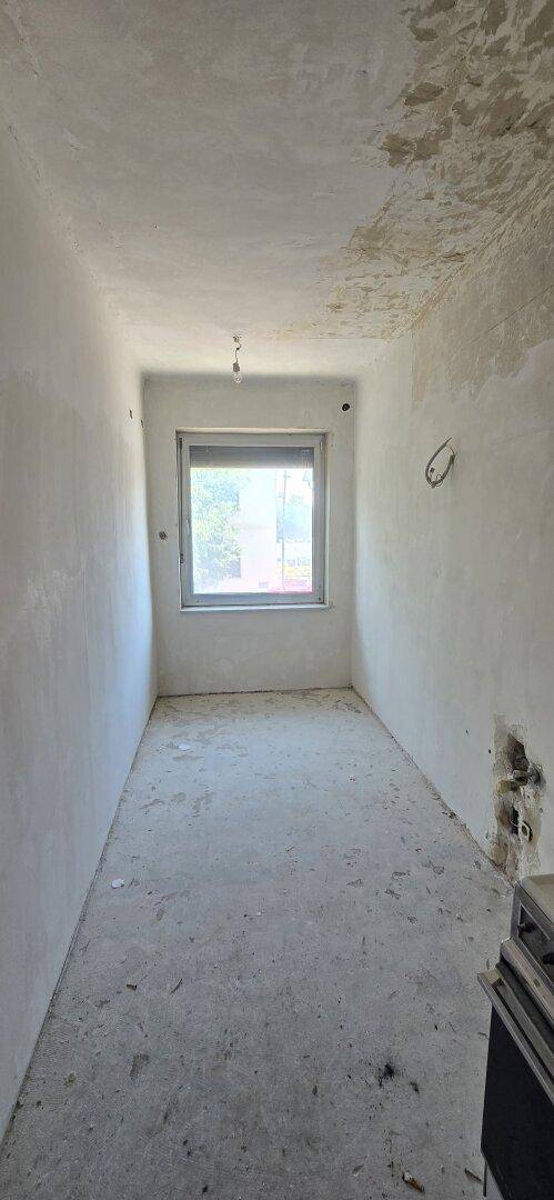 Schmaler, leerer Raum in Renovierung mit Betonboden und einem einzelnen Fenster.
