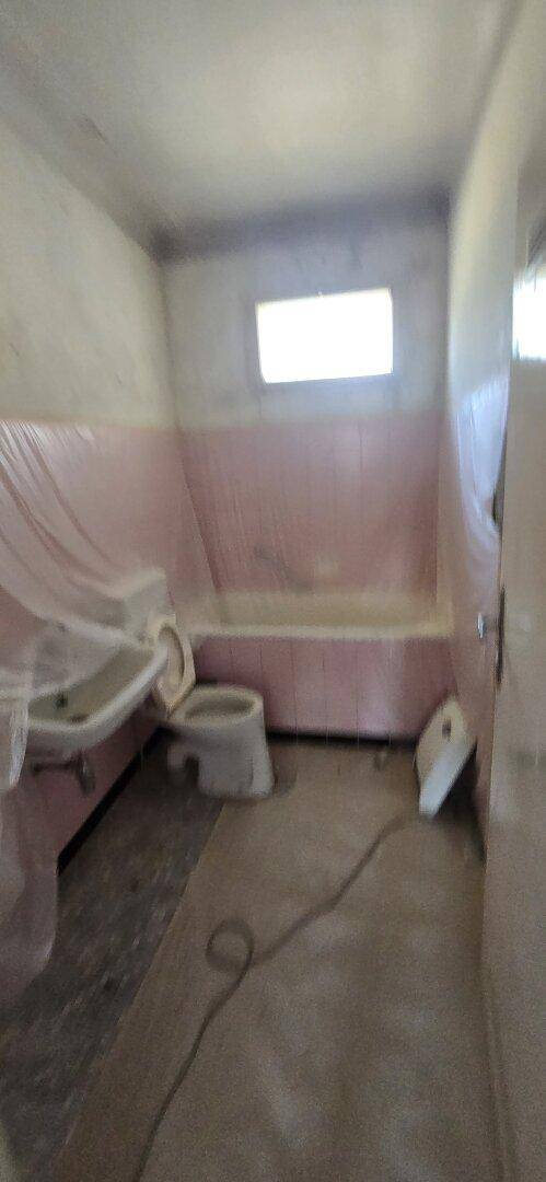 Badezimmer in Renovierung mit rosa Fliesen, Waschbecken und Toilette, alles mit Schutzfolie abgedeckt.