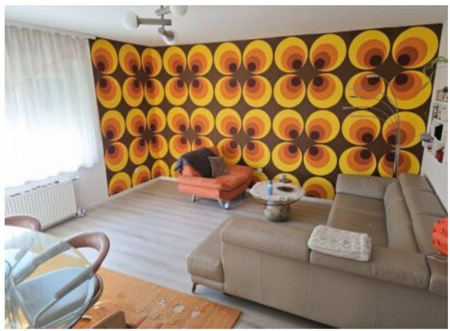 Wohnzimmer mit auffälliger Retro-Tapete, beigem Sofa und hellem Laminatboden.
