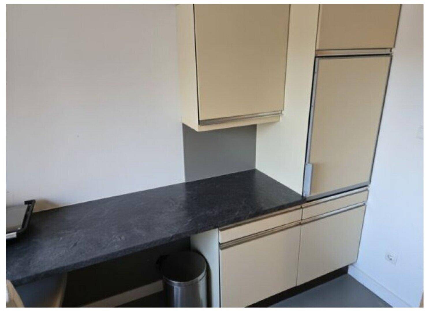 Küchenzeile mit dunkler Arbeitsplatte, beigen Schränken und integriertem Kühlschrank.