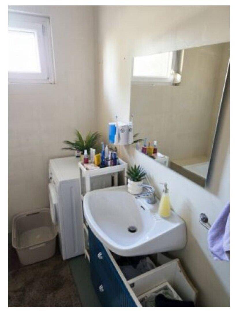 Badezimmer mit Waschbecken, Spiegel und Waschmaschine unter einem kleinen Fenster.