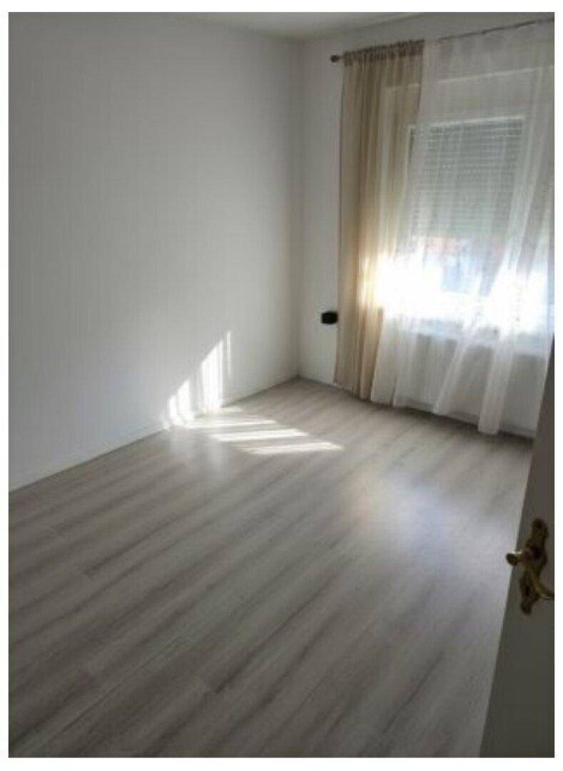 Helles, leeres Zimmer mit Laminatboden und einem Fenster, das viel Tageslicht hereinlässt.