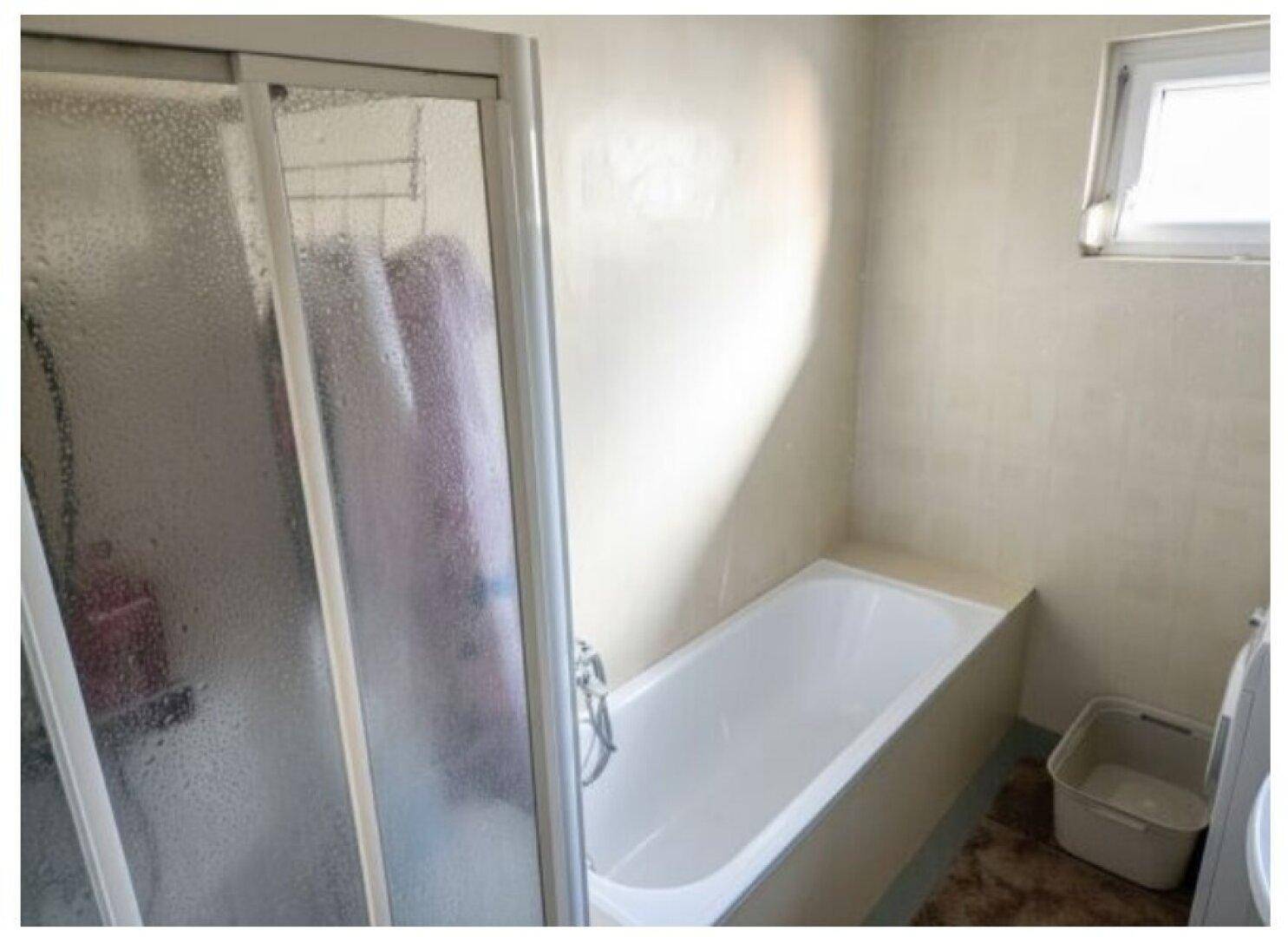 Badezimmer mit Badewanne, Duschkabine und kleinem Fenster für natürliche Belüftung.