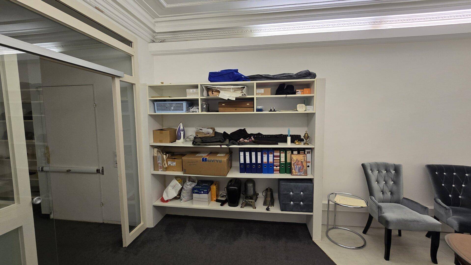 Lagerraum oder Hinterzimmer mit offenen Regalen, Büromaterial und Sitzgelegenheiten.