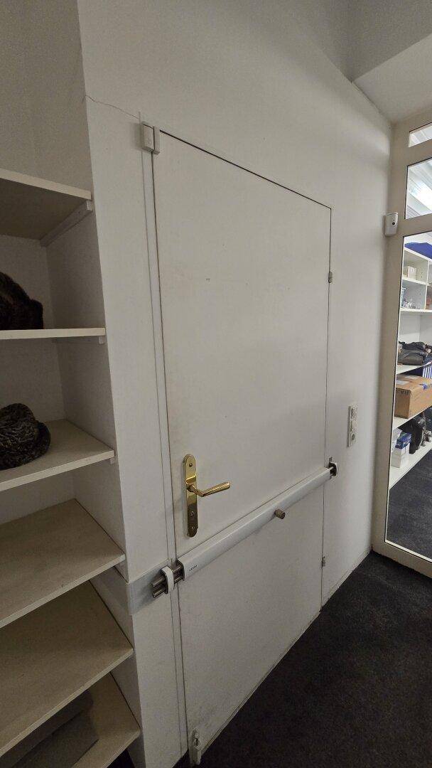 Weiße Tür mit Haltegriff und angrenzenden Regalen, möglicherweise ein Lagerzugang.