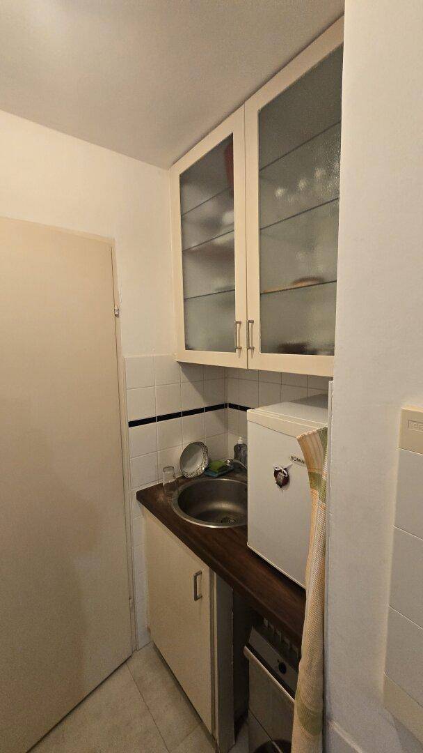 Kleine Küchenzeile mit Spüle, Hängeschränken und einem kleinen Kühlschrank.