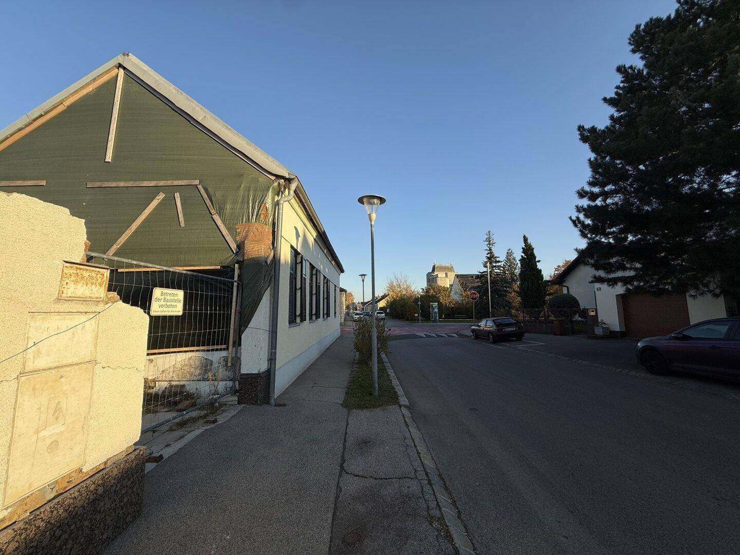 Seitenansicht eines teilweise verkleideten Gebäudes entlang einer ruhigen Straße unter klarem Himmel.