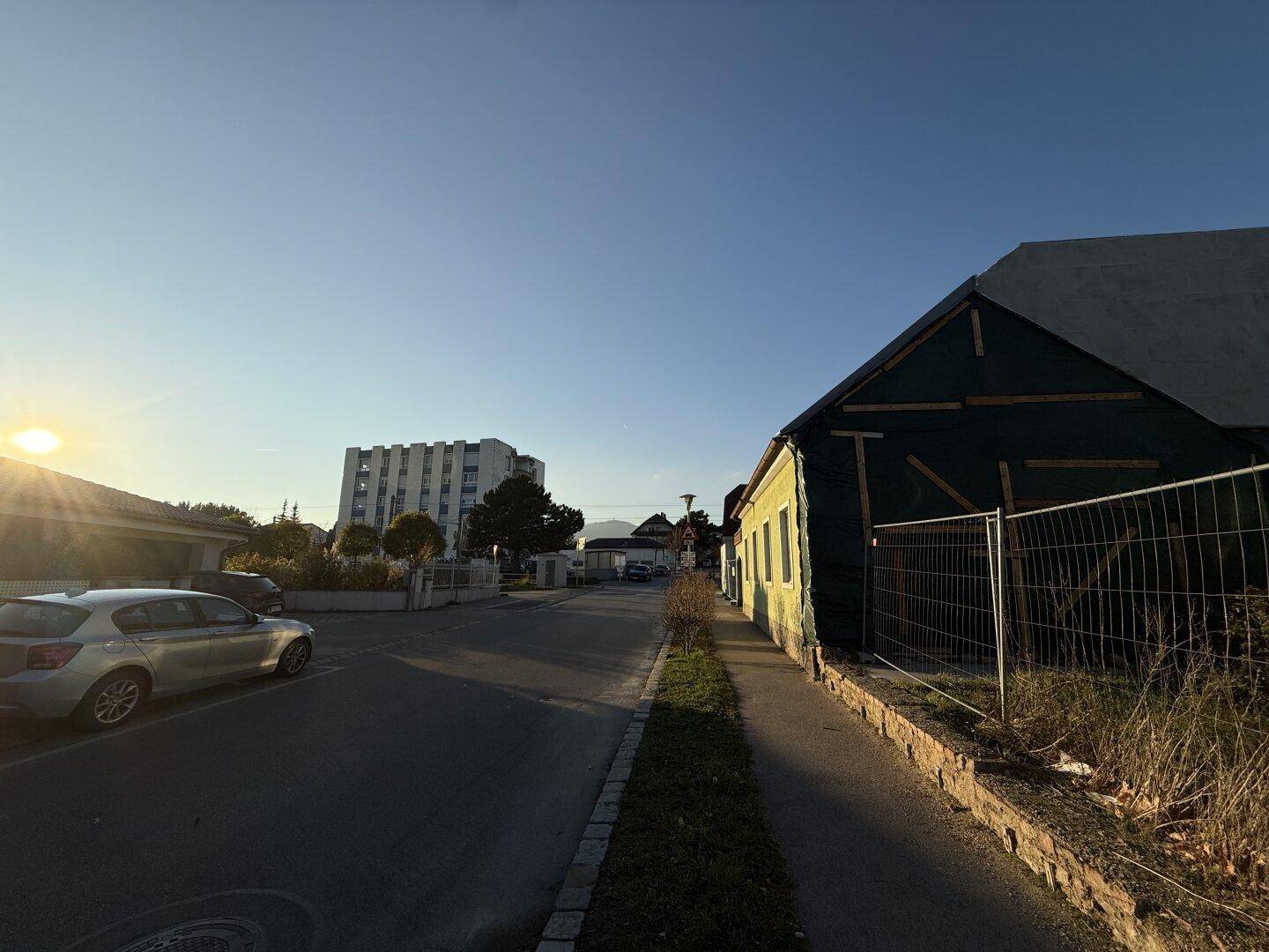 Straßenansicht mit einem teilweise verkleideten Gebäude und einem Wohnblock in der Ferne.