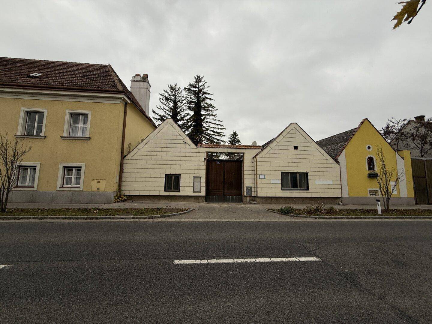 Fassade eines Gebäudes mit zentralem Holztor und angrenzenden gelben Häusern unter bewölktem Himmel.