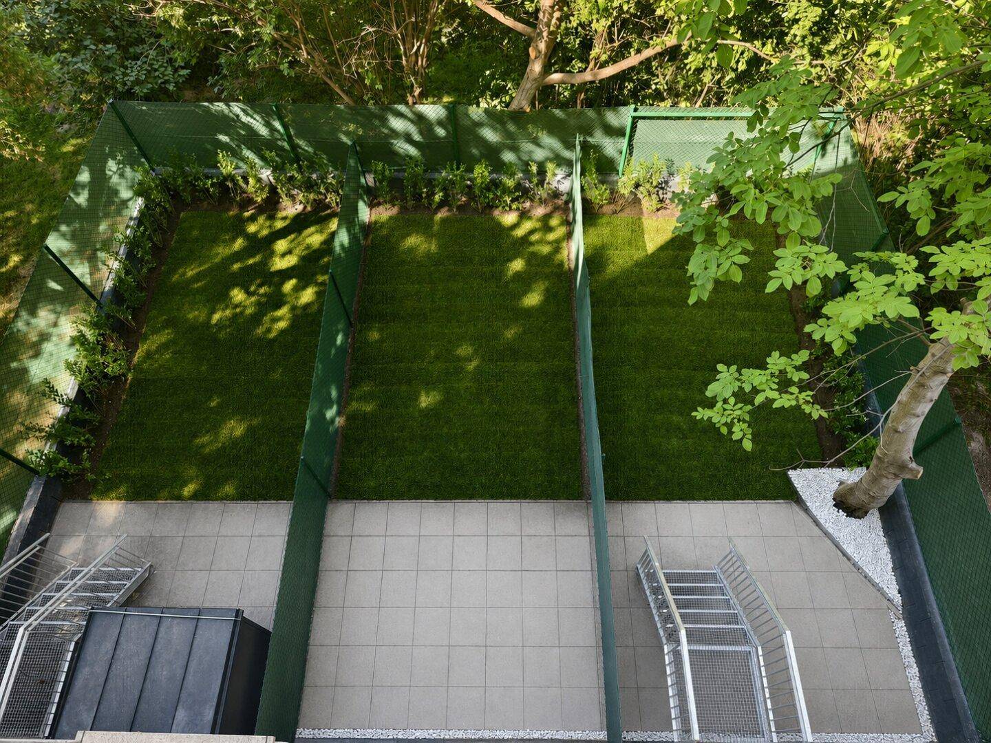 Vogelperspektive auf mehrere kleine Gartenparzellen mit Kunstrasen, umgeben von grünen Zäunen und Bäumen.