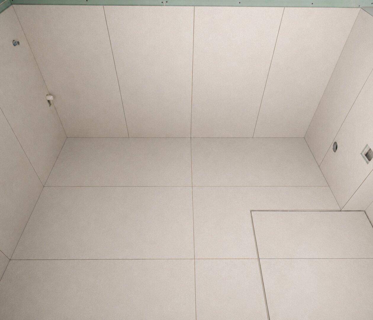 Unfertiger Raum mit vollständig gefliesten Wänden und Boden, möglicherweise ein Duschbereich oder kleines Badezimmer.