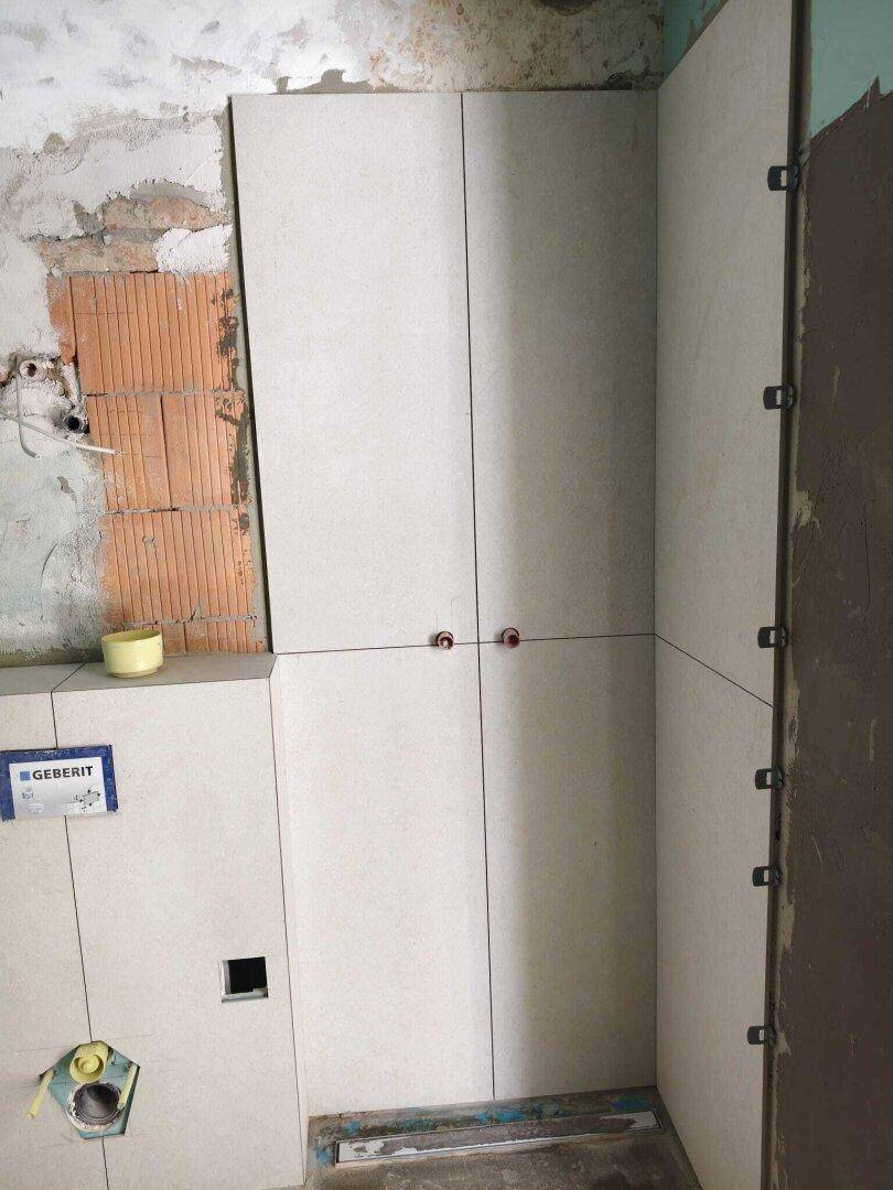 Badezimmer im Bau mit teilweise gefliesten Wänden, sichtbaren Ziegeln und Installationen für die Toilette.