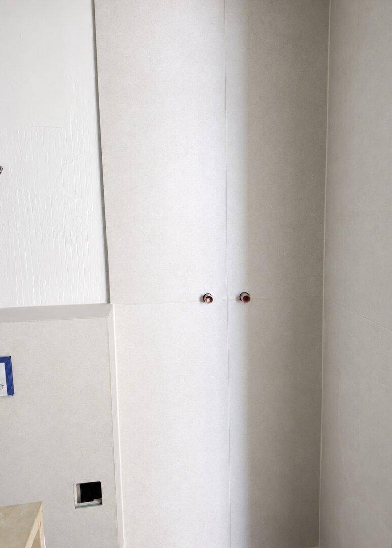 Wandbereich in einem Badezimmer im Rohbau mit sichtbaren Wasseranschlüssen und hellen Fliesen.