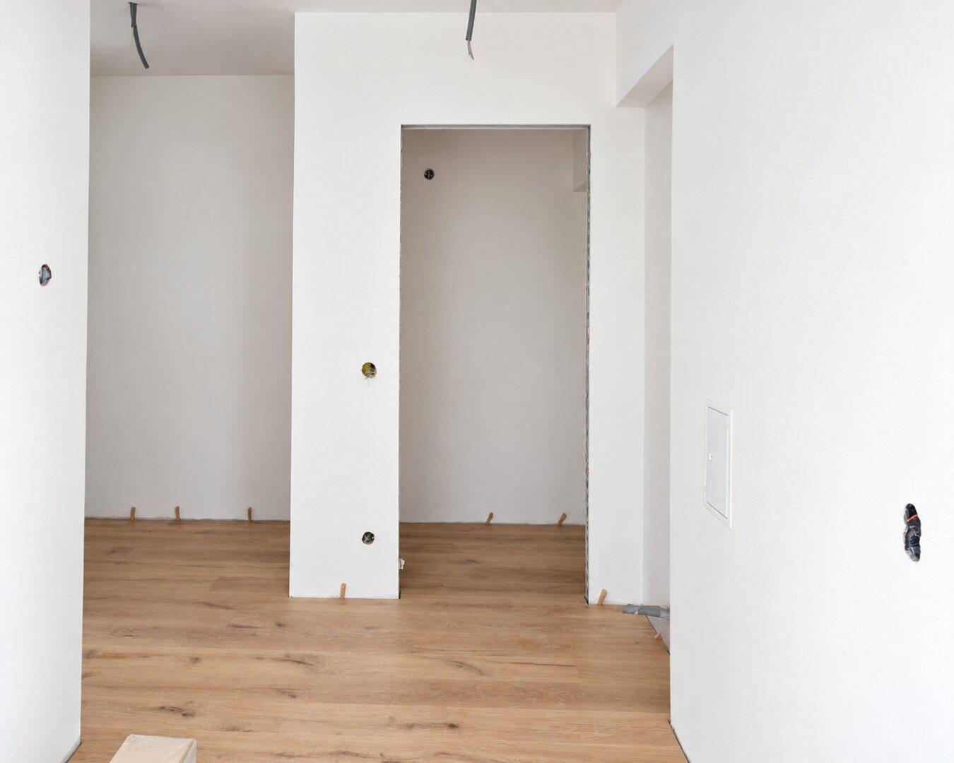 Heller Innenraum im Rohbau mit weißen Wänden und neu verlegtem Holzplankenboden, bereit für den Ausbau.