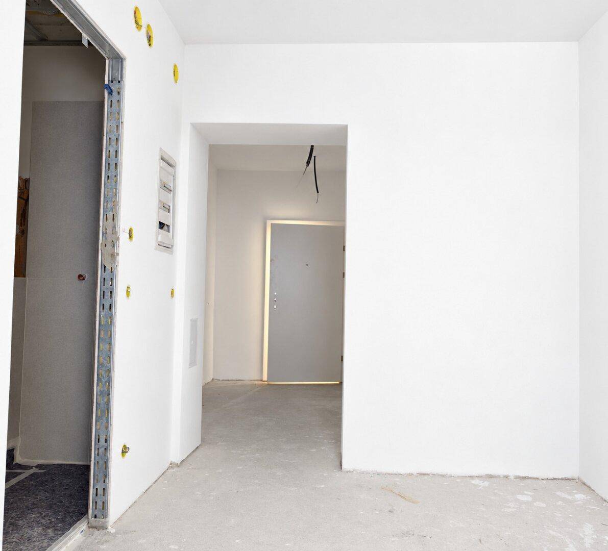 Eingangsbereich im Neubau mit Betonboden und weißer Eingangstür, noch unfertig.