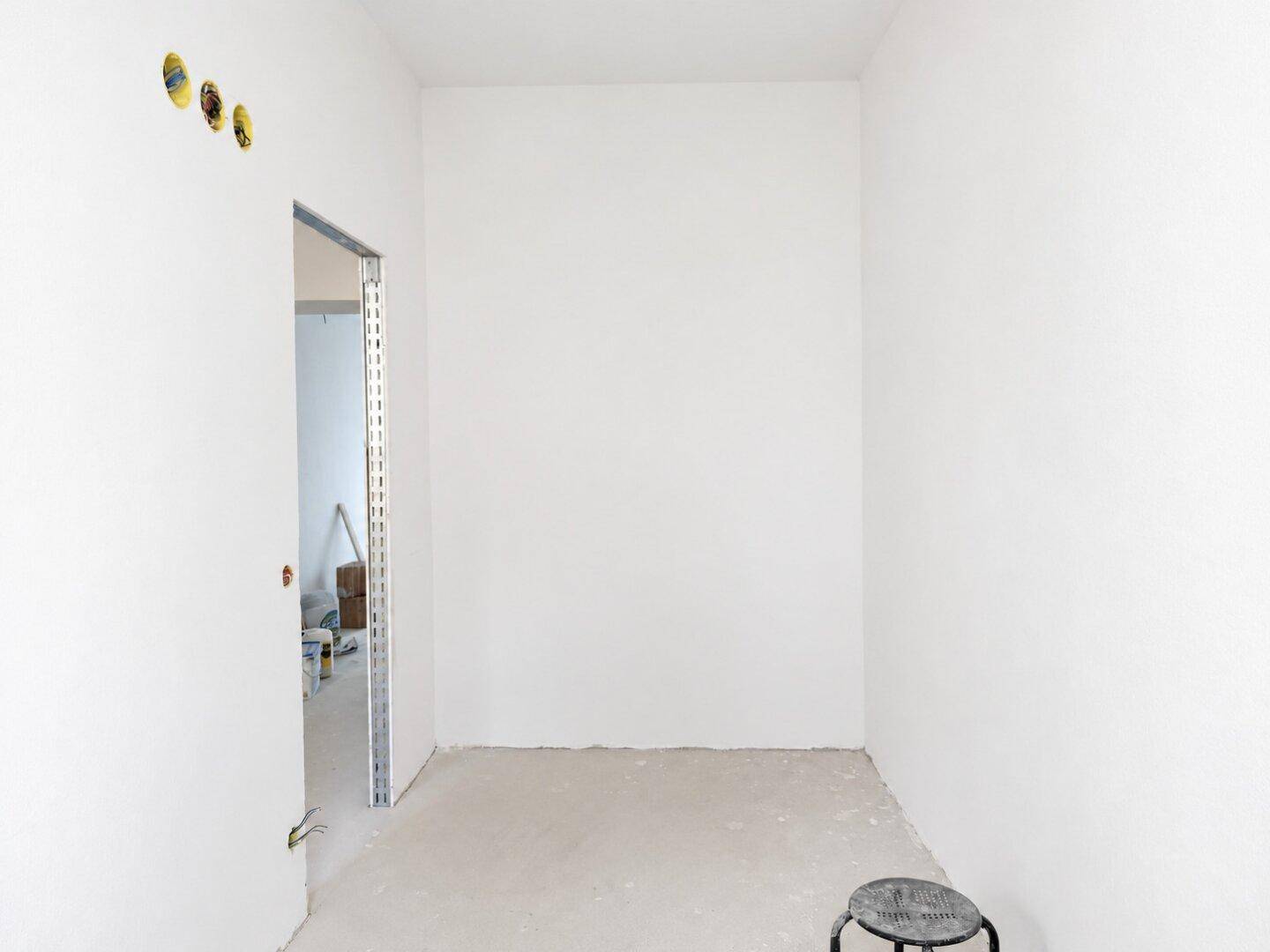 Leerer Raum im Neubau mit weißen Wänden und Betonboden, bereit für den Innenausbau.