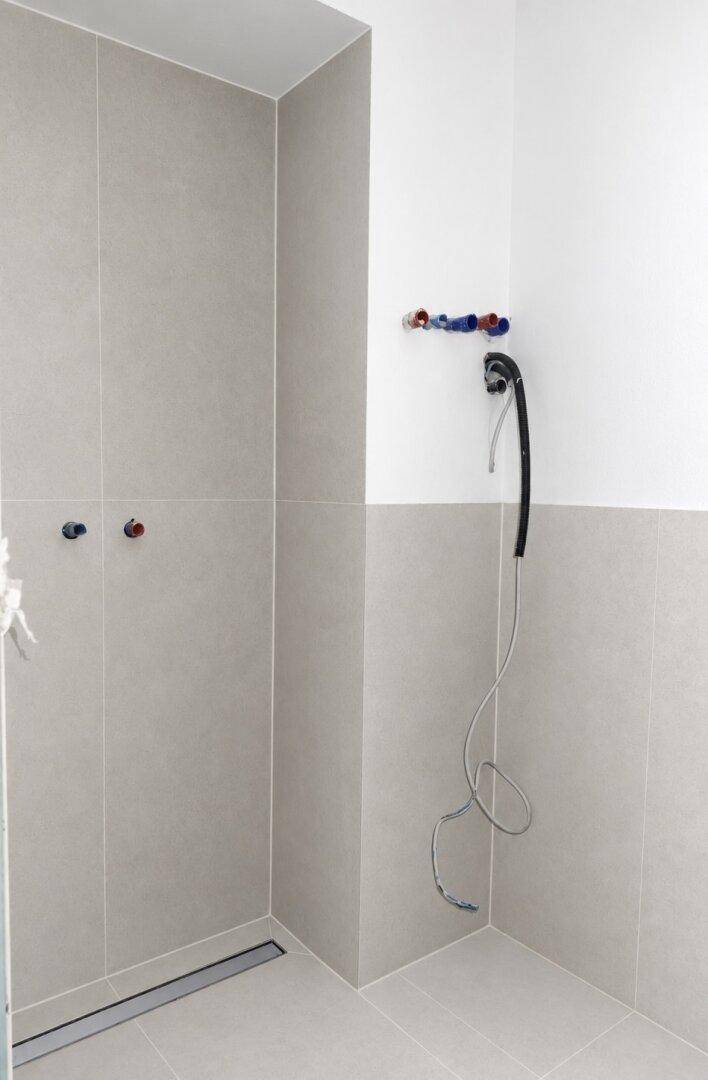 Duschbereich im Badezimmer mit modernen grauen Fliesen und vorbereiteten Anschlüssen.