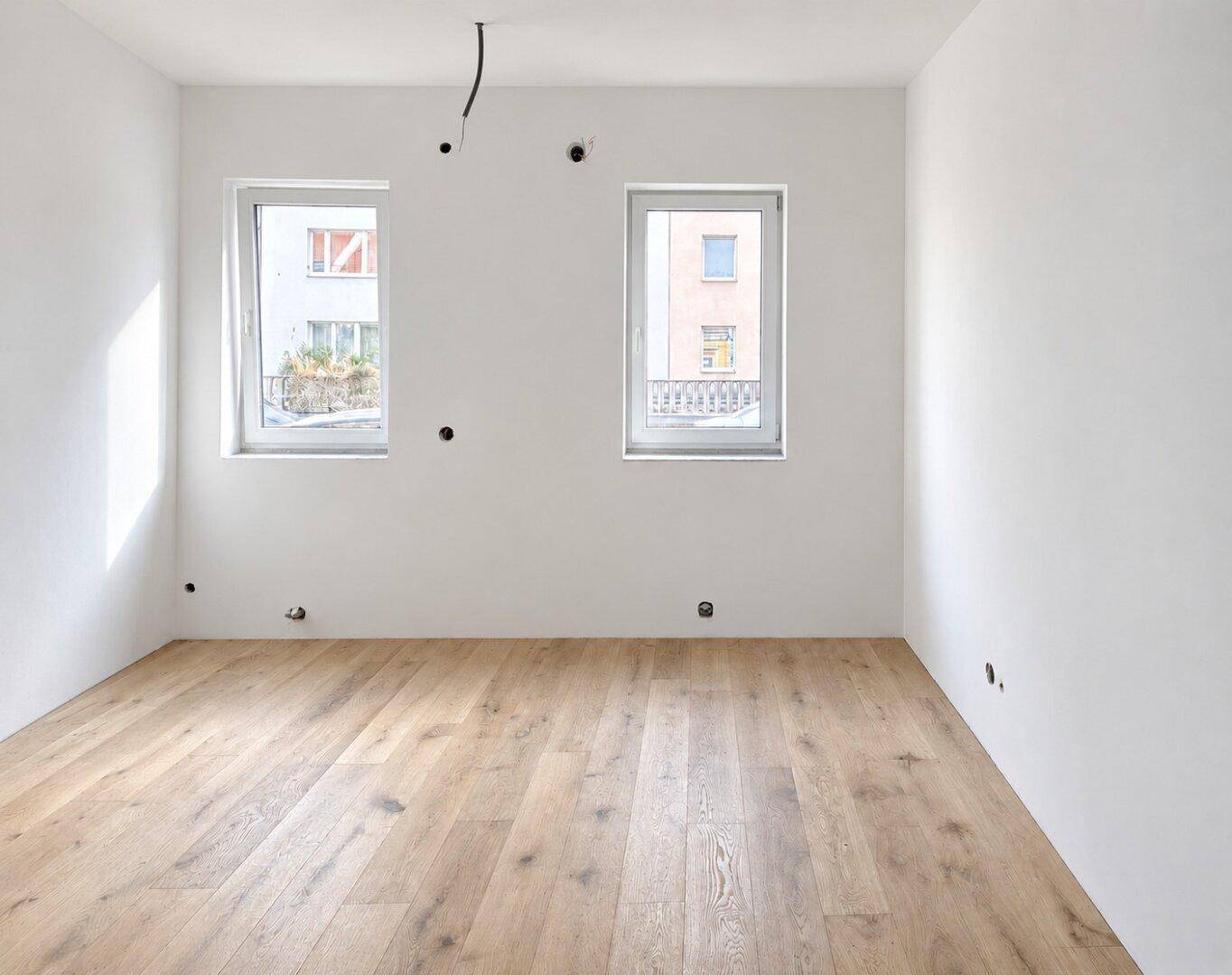 Unmöblierter Raum im Neubau mit Holzboden und Fenstern mit Blick auf den Innenhof.