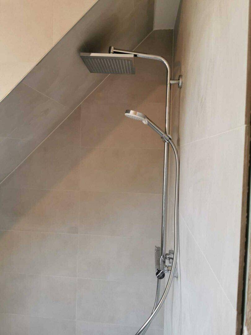 Moderne Regendusche und Handbrause in einem gefliesten Badezimmer mit Dachschräge.