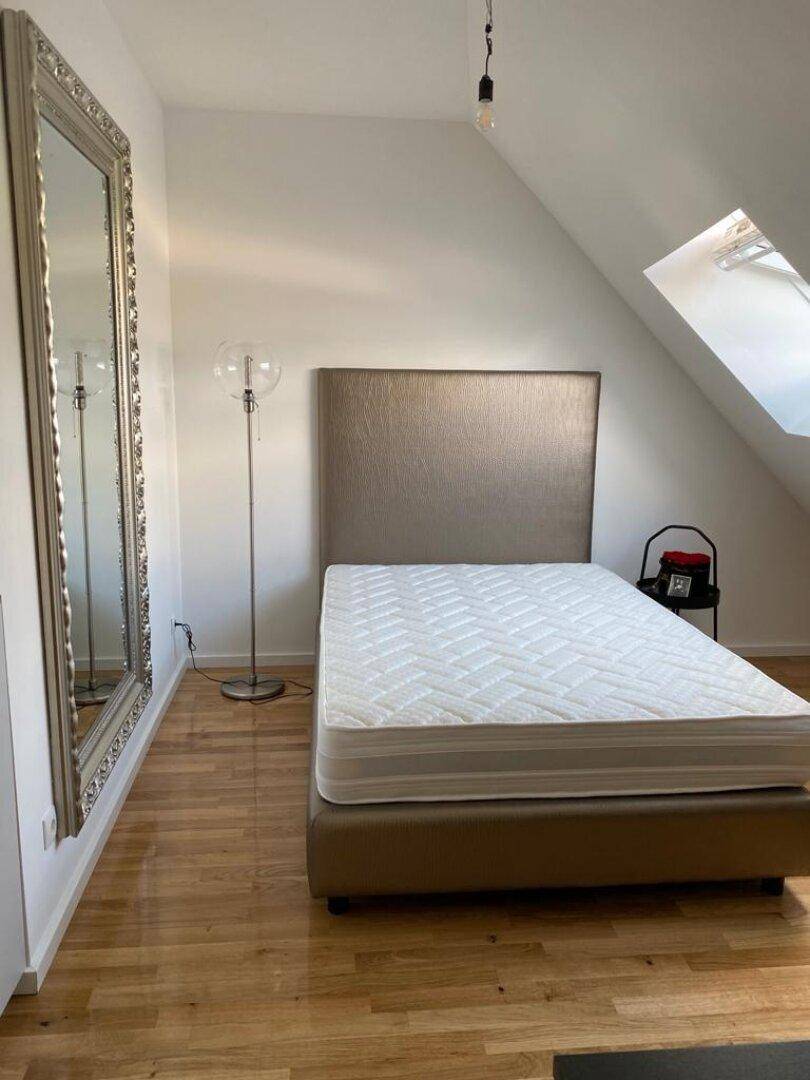 Schlafzimmer mit Holzboden, großem Spiegel und Dachfenster unter der Schräge.