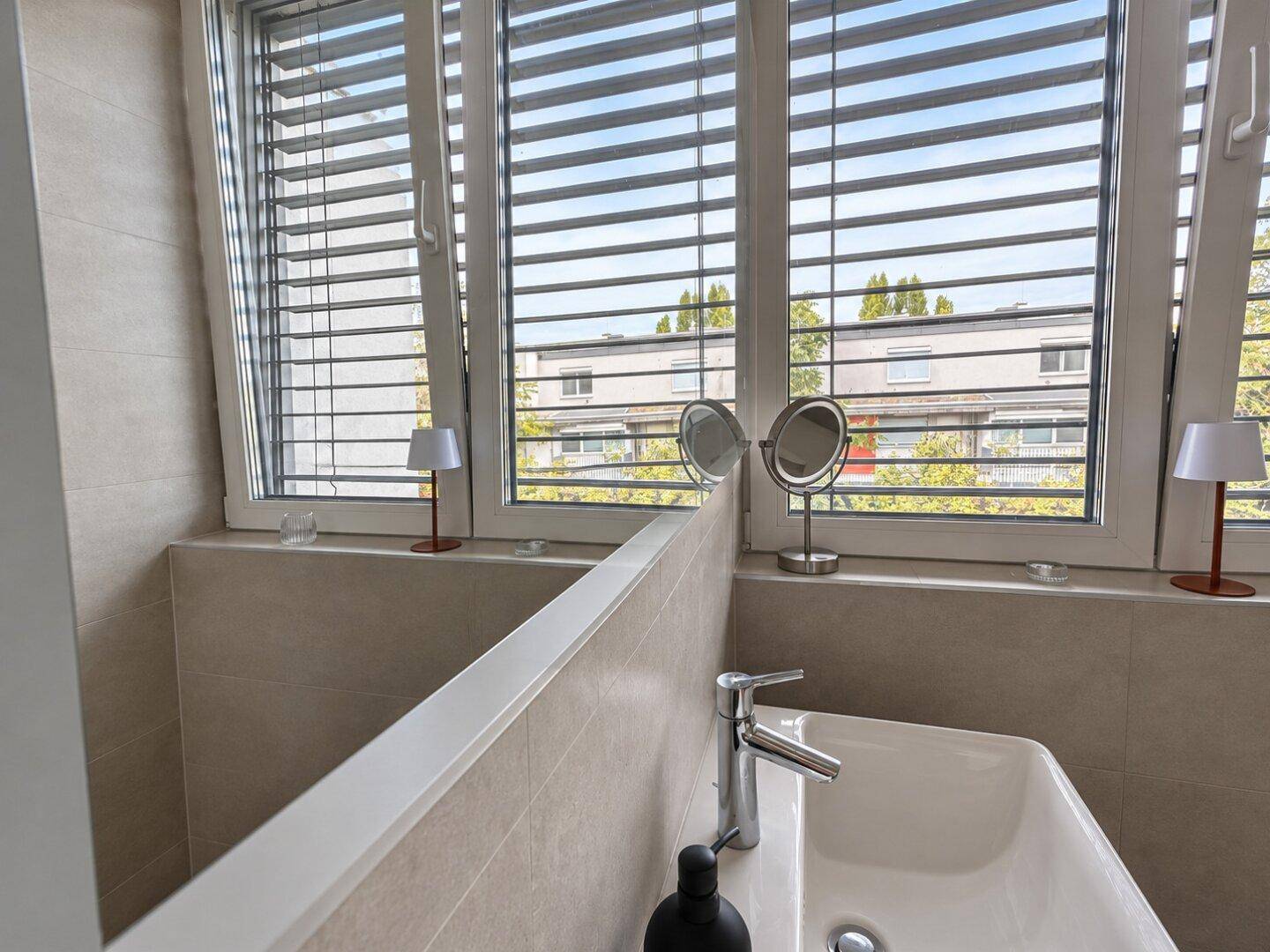 Badezimmer mit Einzelwaschbecken, Spiegel und großem Fenster für natürliches Licht.