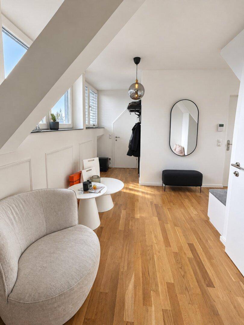 Heller Flurbereich mit Holzboden, gemütlichem Sessel und modernem Spiegel.