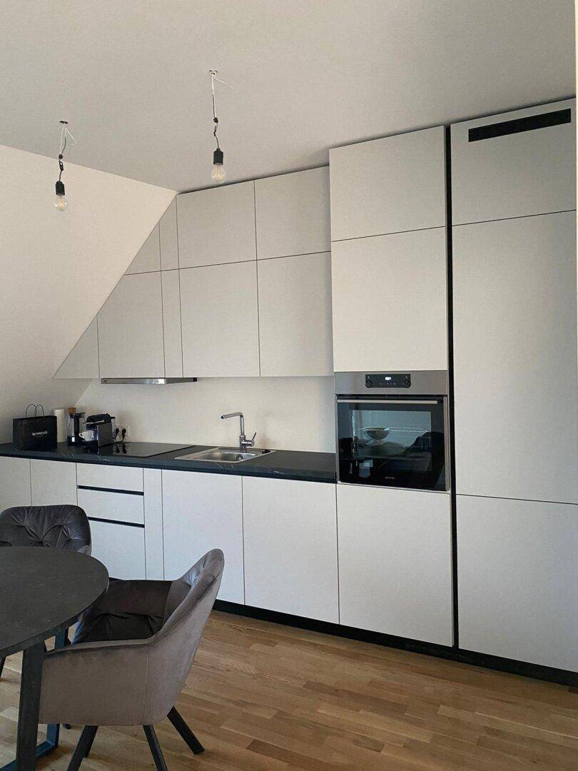 Moderne Küche mit hellgrauen Schränken, schwarzer Arbeitsplatte und integriertem Backofen.