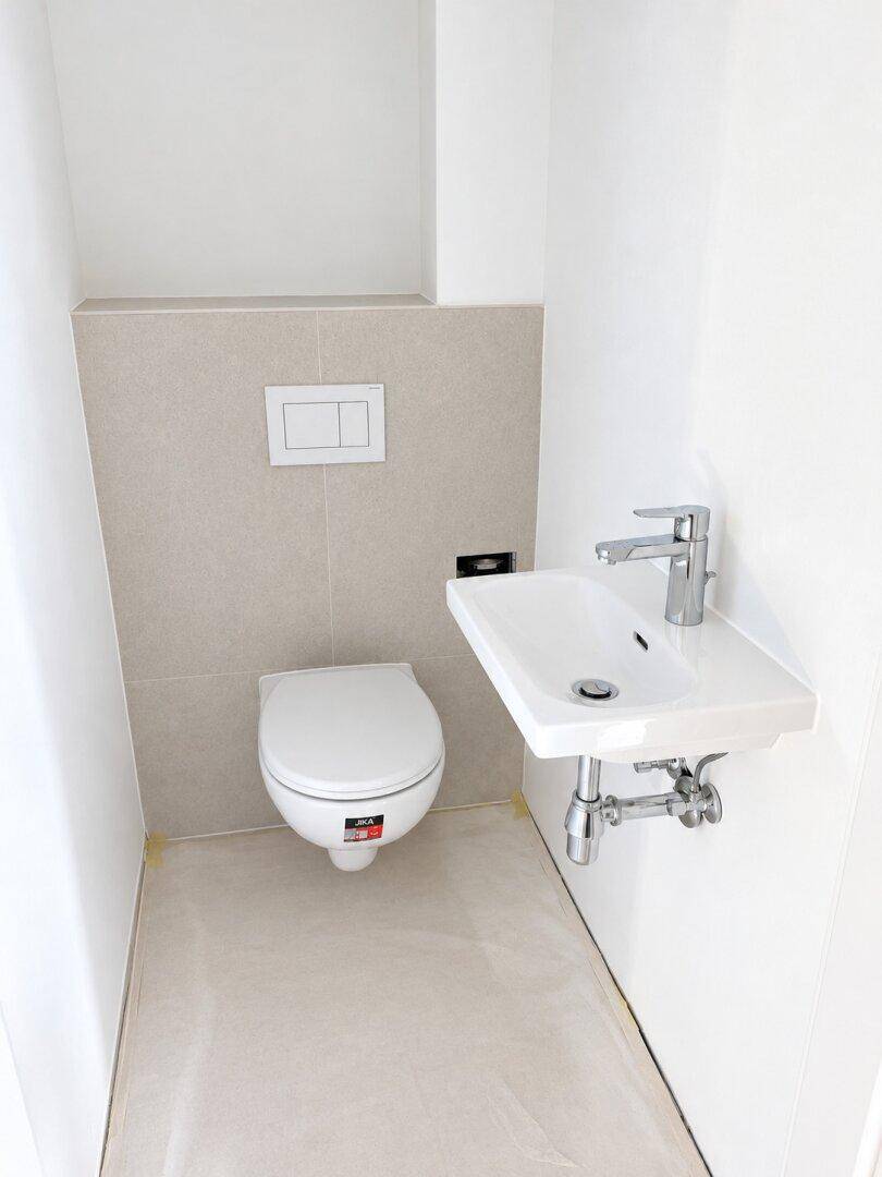Kompaktes Gäste-WC mit wandhängender Toilette und kleinem Waschbecken in hellen Farbtönen.