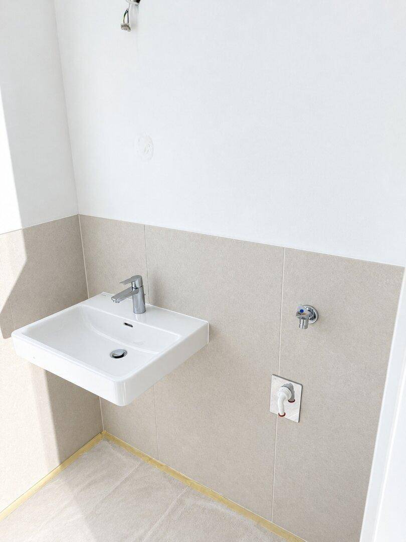 Helles Badezimmer mit modernem, wandmontiertem Waschbecken und beigefarbenen Wandfliesen.