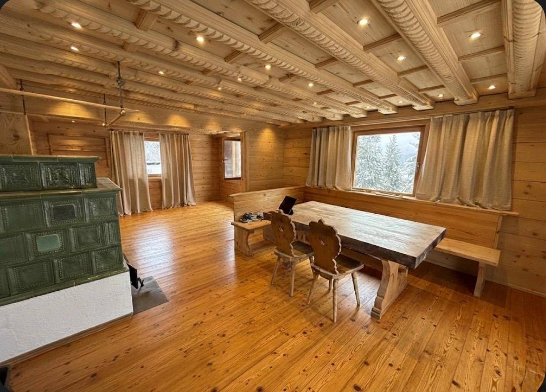 Gemütlicher Wohn- und Essbereich mit Holzboden, Holzwänden, Holzbalkendecke und einem traditionellen Kachelofen.