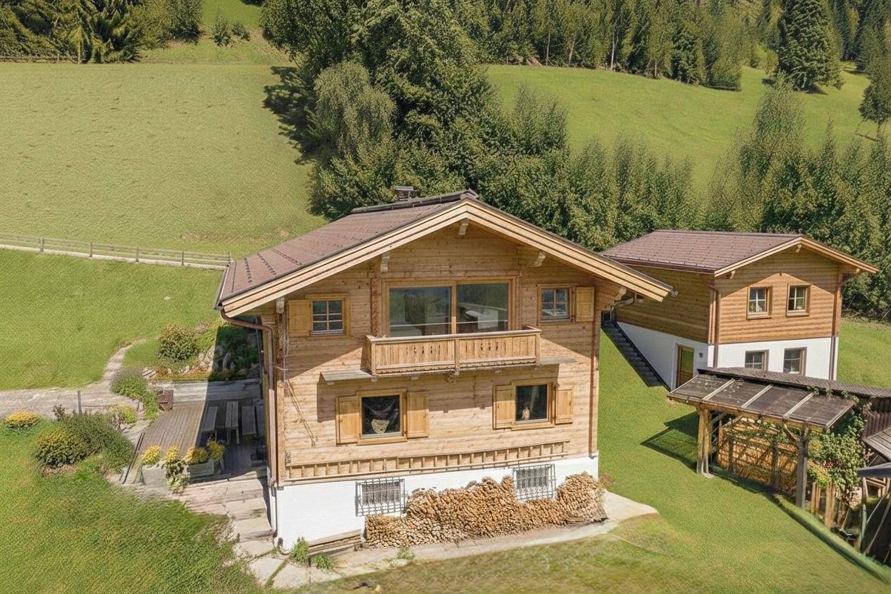 Luftaufnahme eines traditionellen Holzhauses mit Satteldach und einem Nebengebäude in grüner Hanglage.