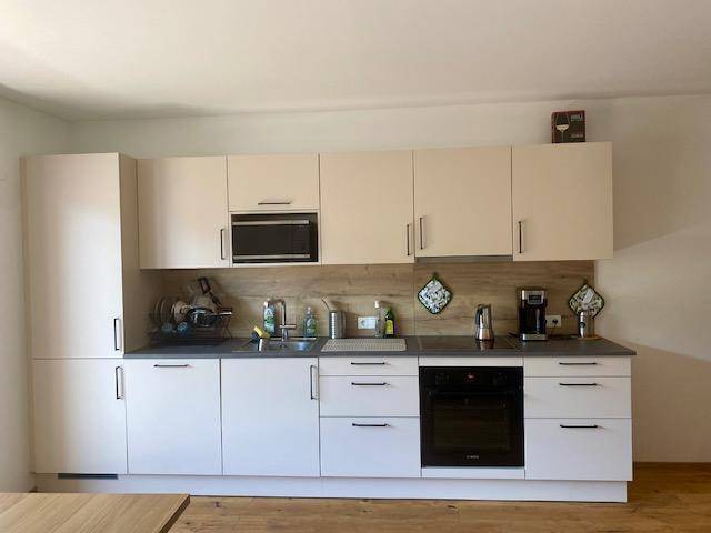 Moderne Einbauküche mit hellen Schränken, integrierten Geräten und einer Arbeitsplatte in dunklem Grau.