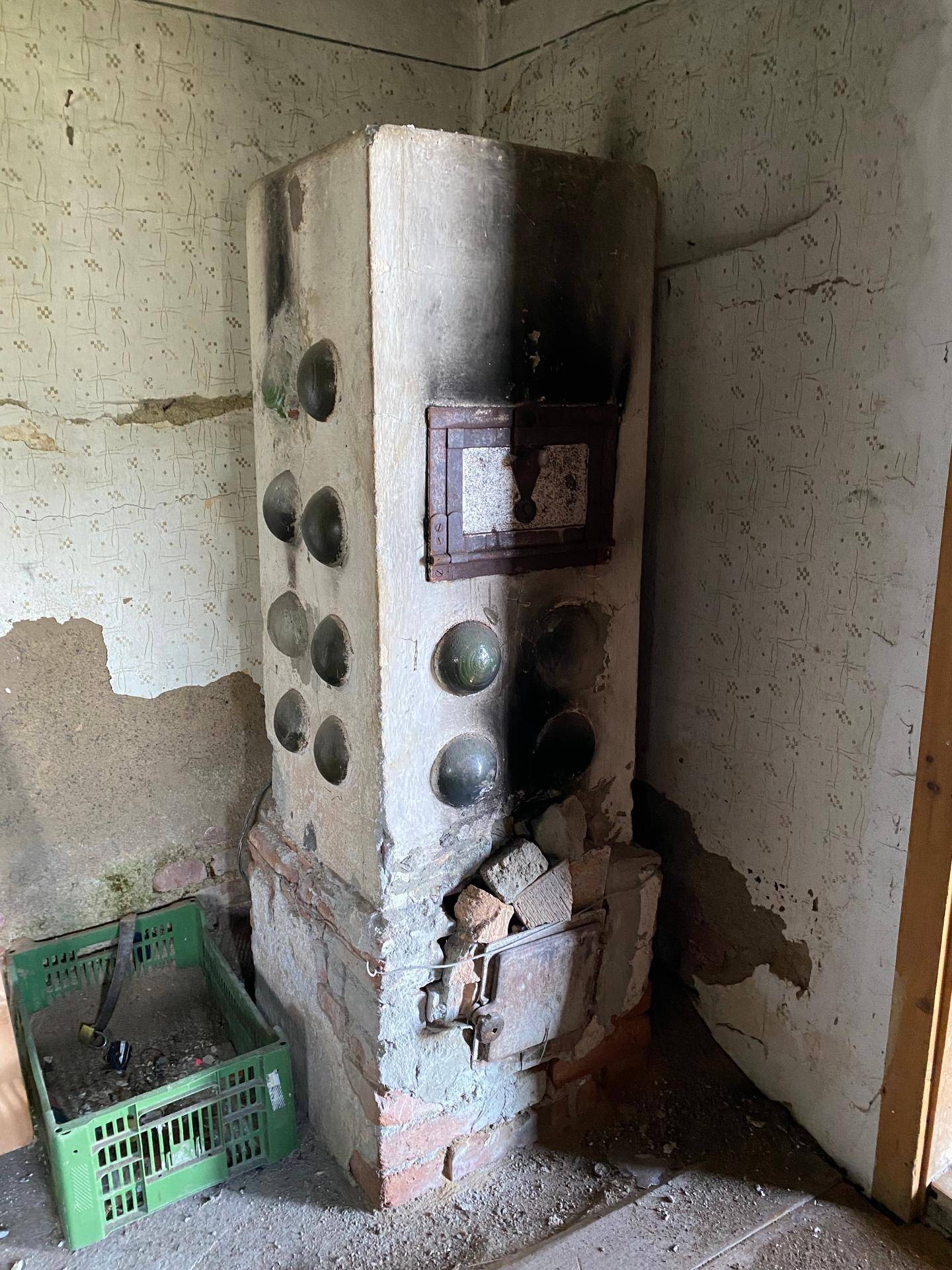 Alter Ofen in einem Raum mit abgenutzter Tapete und sichtbaren Ziegeln.