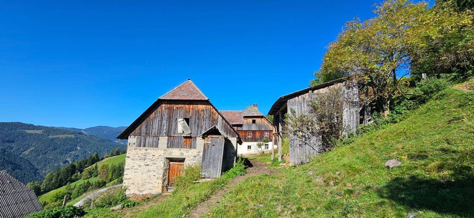 Ensemble ländlicher Gebäude mit Holzfassaden und Steinsockeln in einer idyllischen Berglandschaft.
