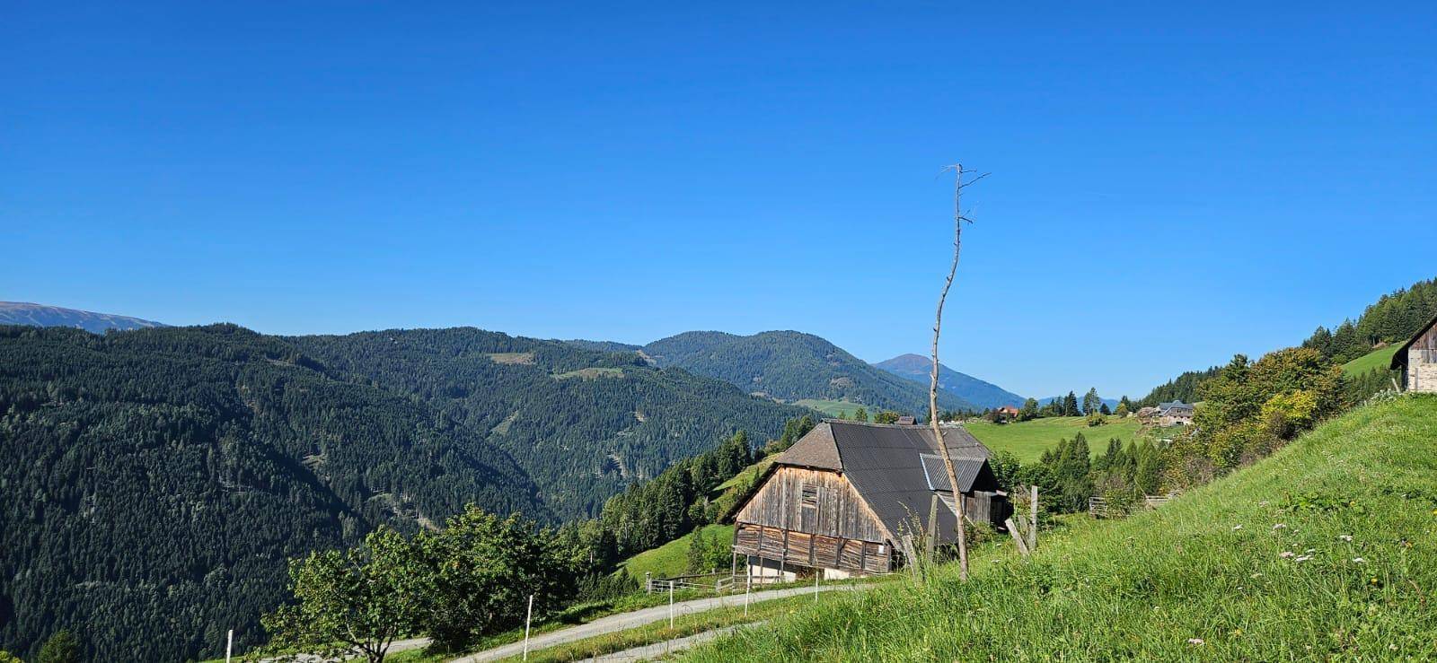Ländliches Haus mit Holzbalken und Schindeldach, eingebettet in eine weite grüne Landschaft.
