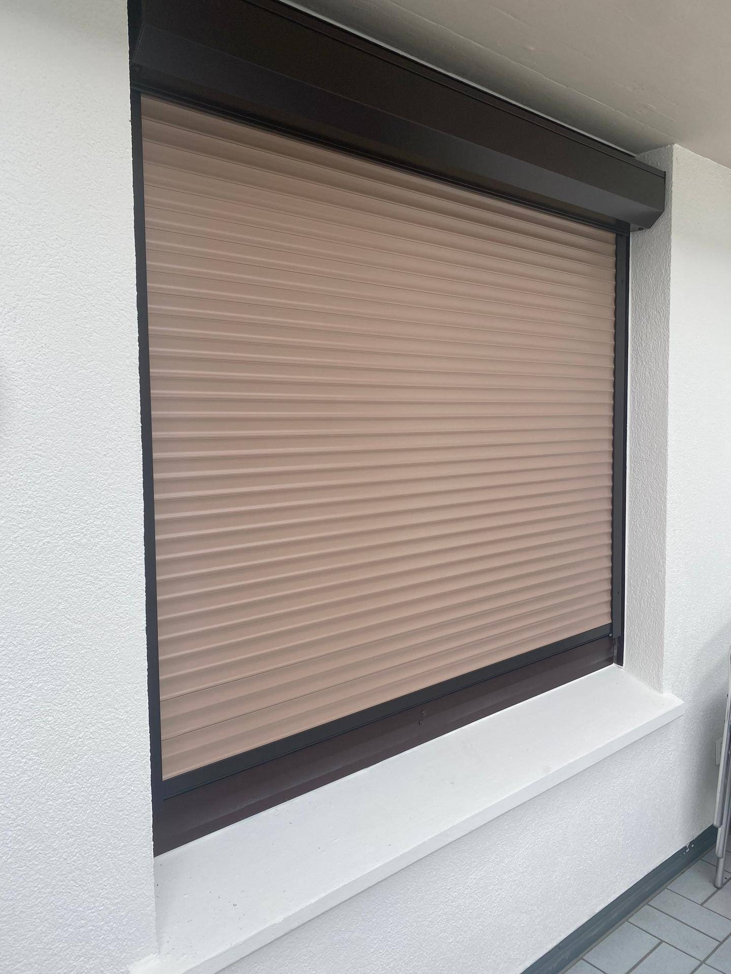 Nahaufnahme eines Fensters mit geschlossenem Rollladen in beiger Farbe.