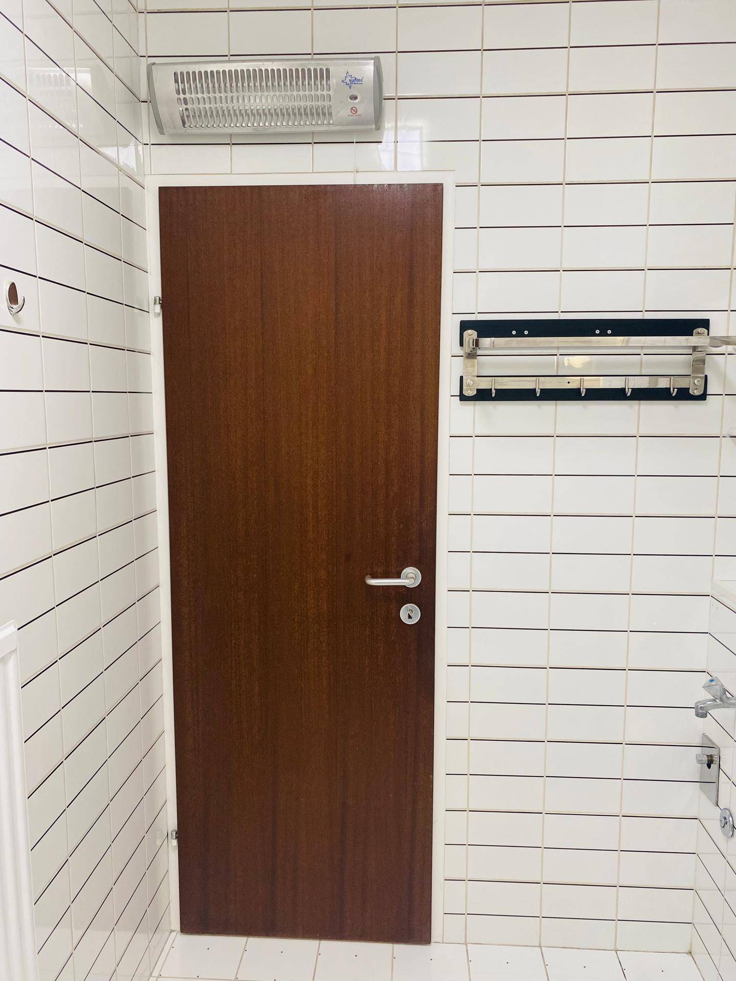 Badezimmertür in einem Raum mit weißen Fliesen und einem Abluftventilator an der Decke.