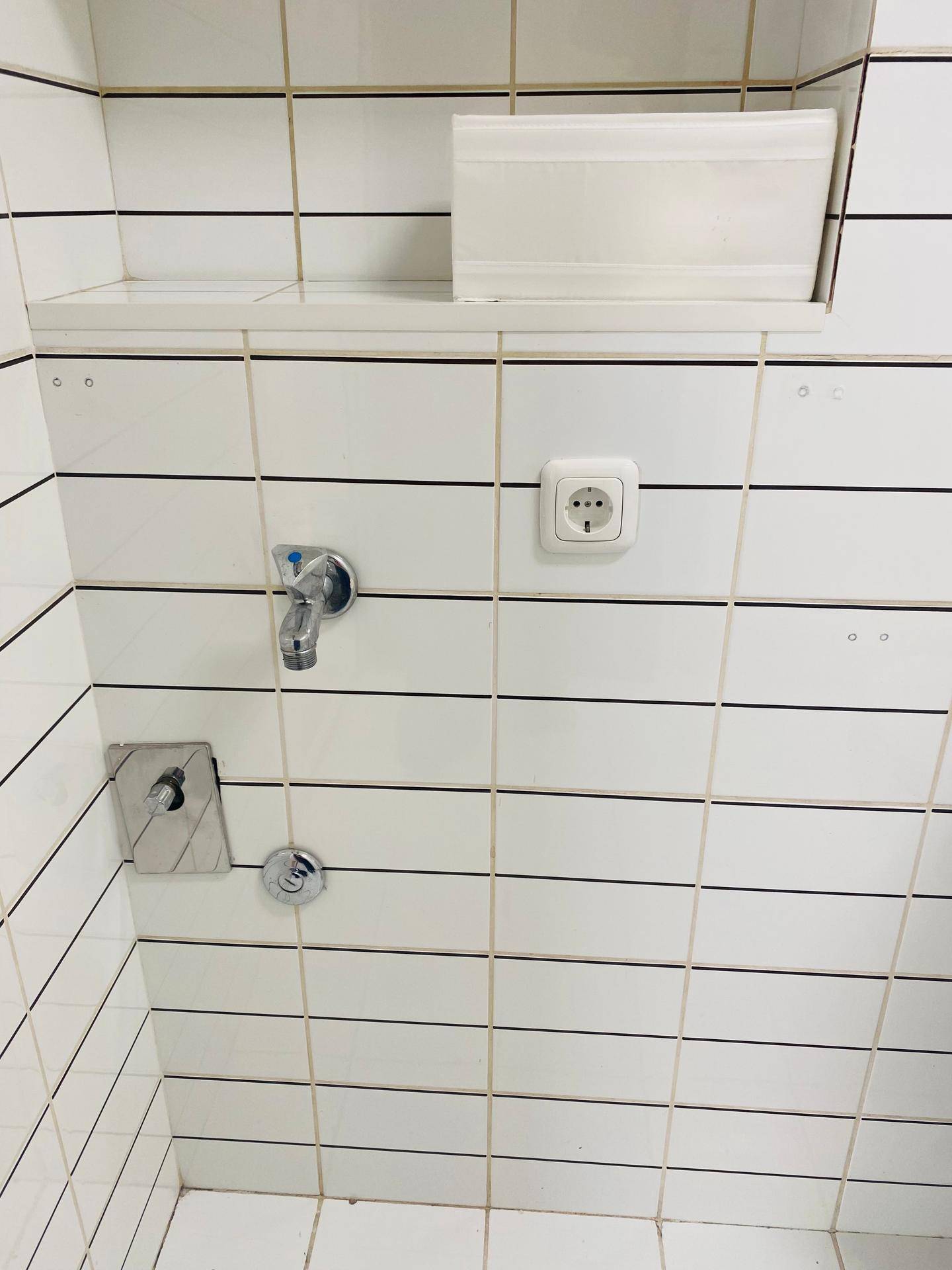 Nahaufnahme einer weiß gefliesten Wand im Badezimmer mit Wasseranschluss und Steckdose.