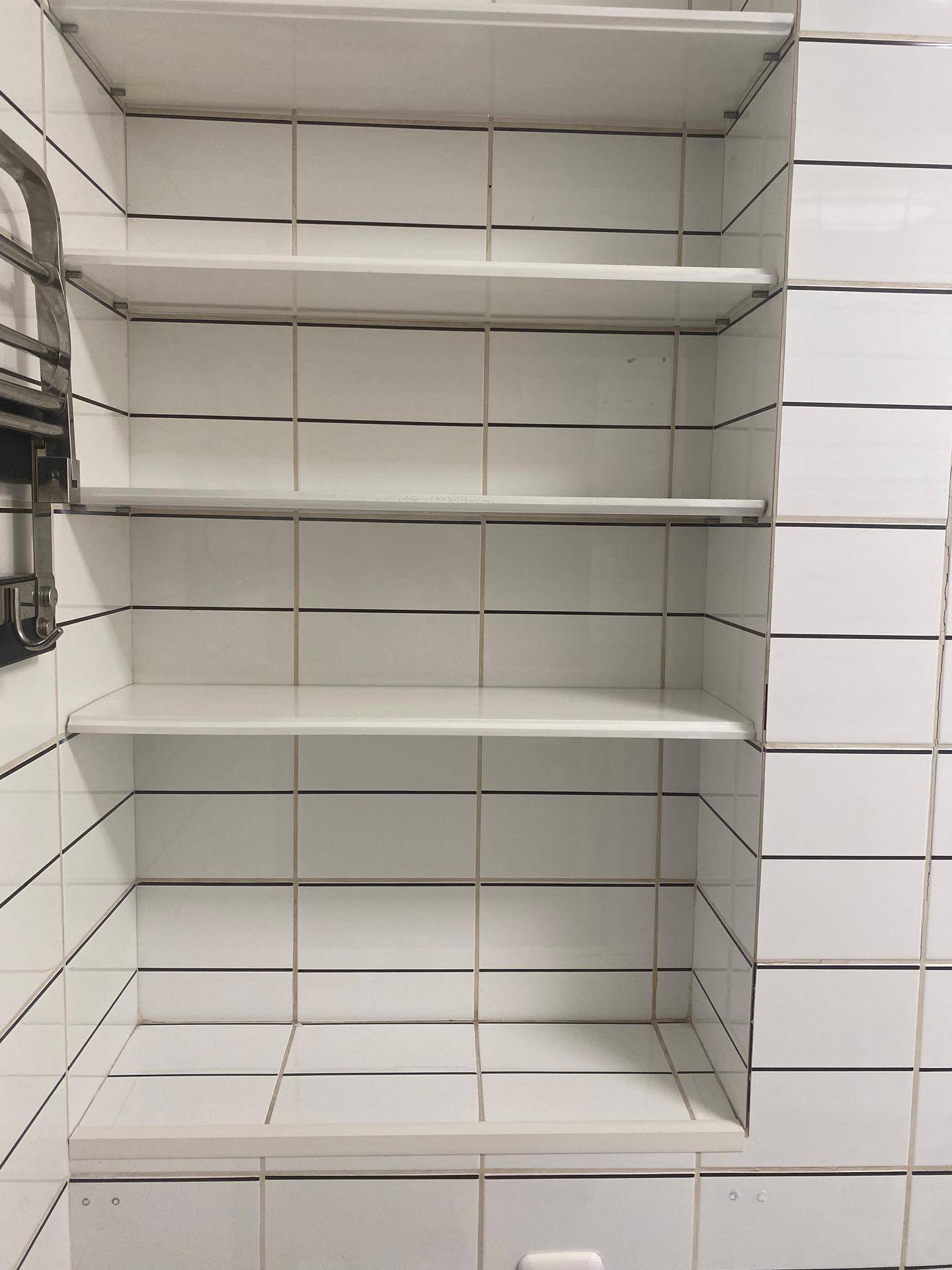 Weiße geflieste Wand mit praktischen Ablageflächen in einem Badezimmer oder Abstellraum.
