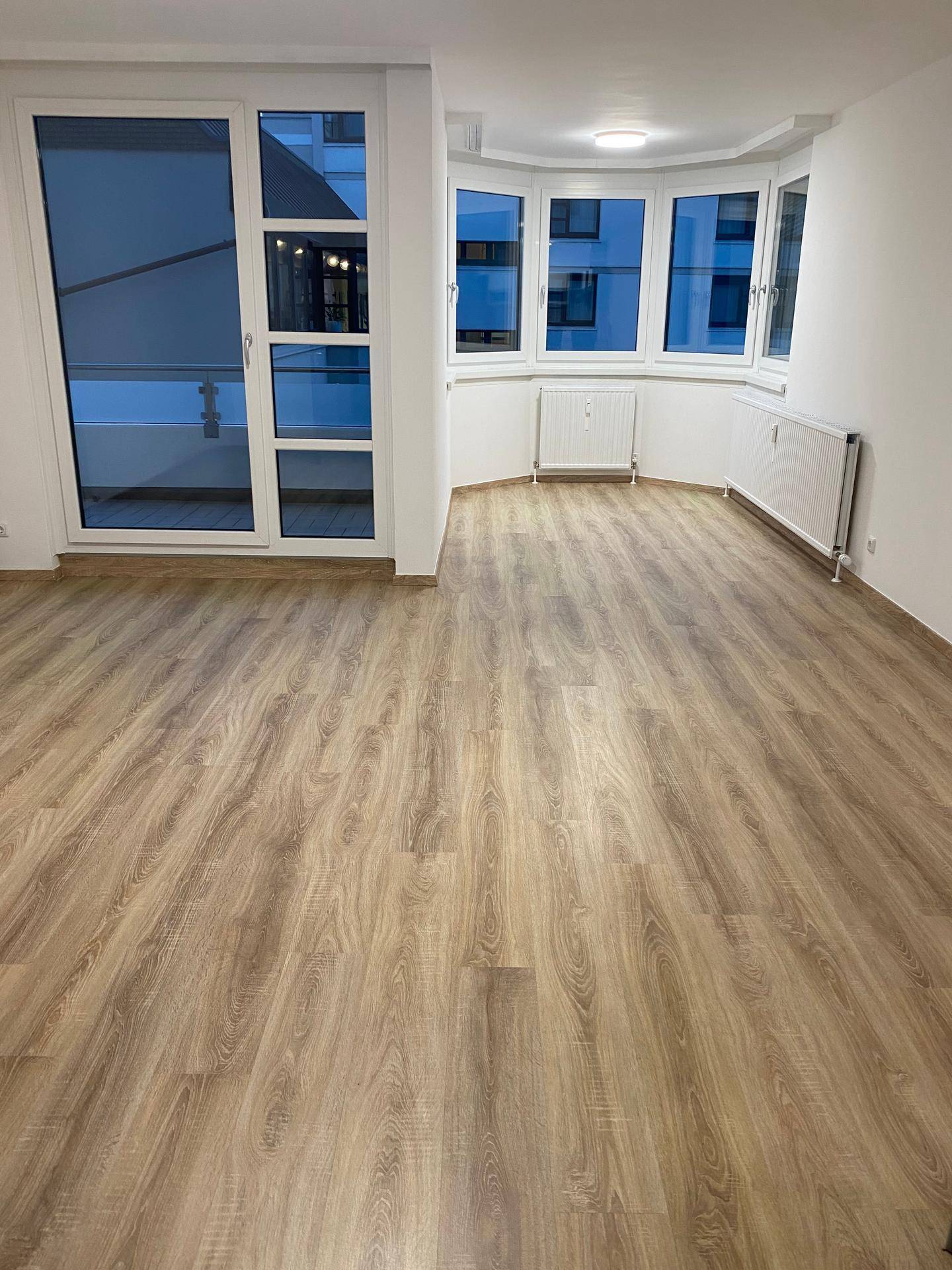Geräumiges Wohnzimmer mit Laminatboden, Erkerfenstern und Zugang zu einem Balkon.