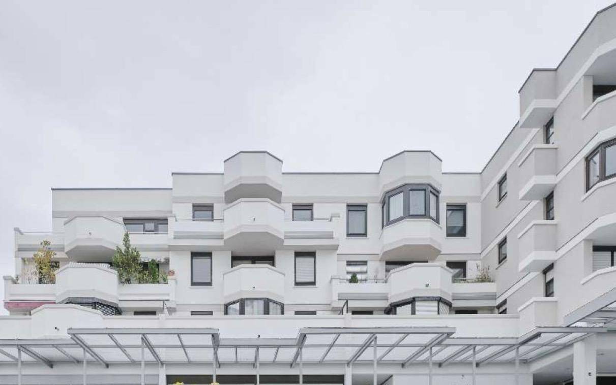 Moderne Fassade eines Mehrfamilienhauses mit zahlreichen Balkonen und klaren Linien.