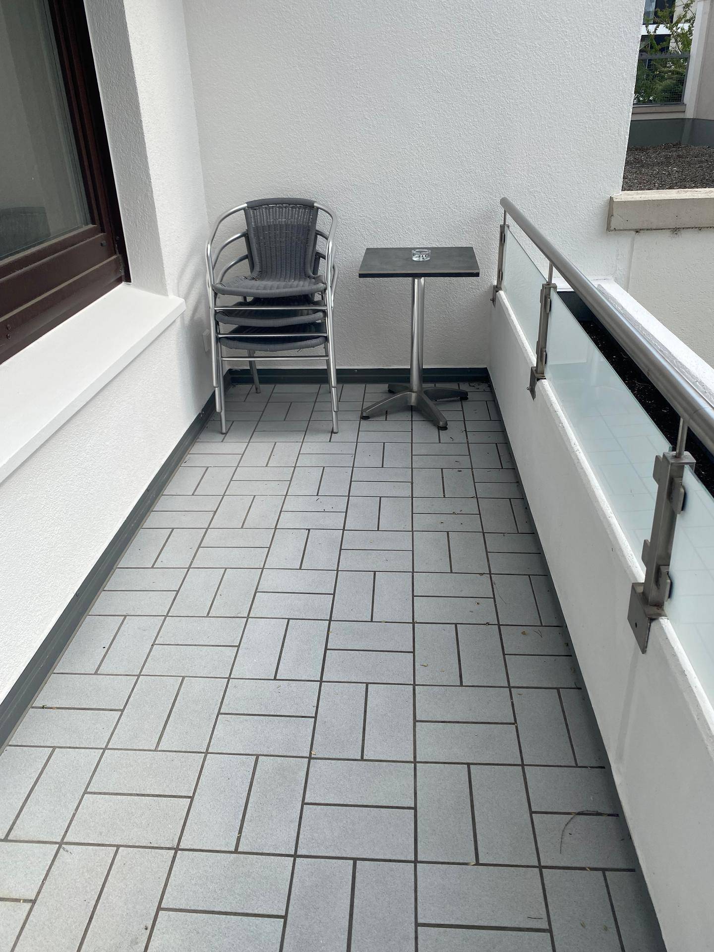 Balkon mit grauen Fliesen und einfacher Bestuhlung, ideal für entspannte Stunden im Freien.