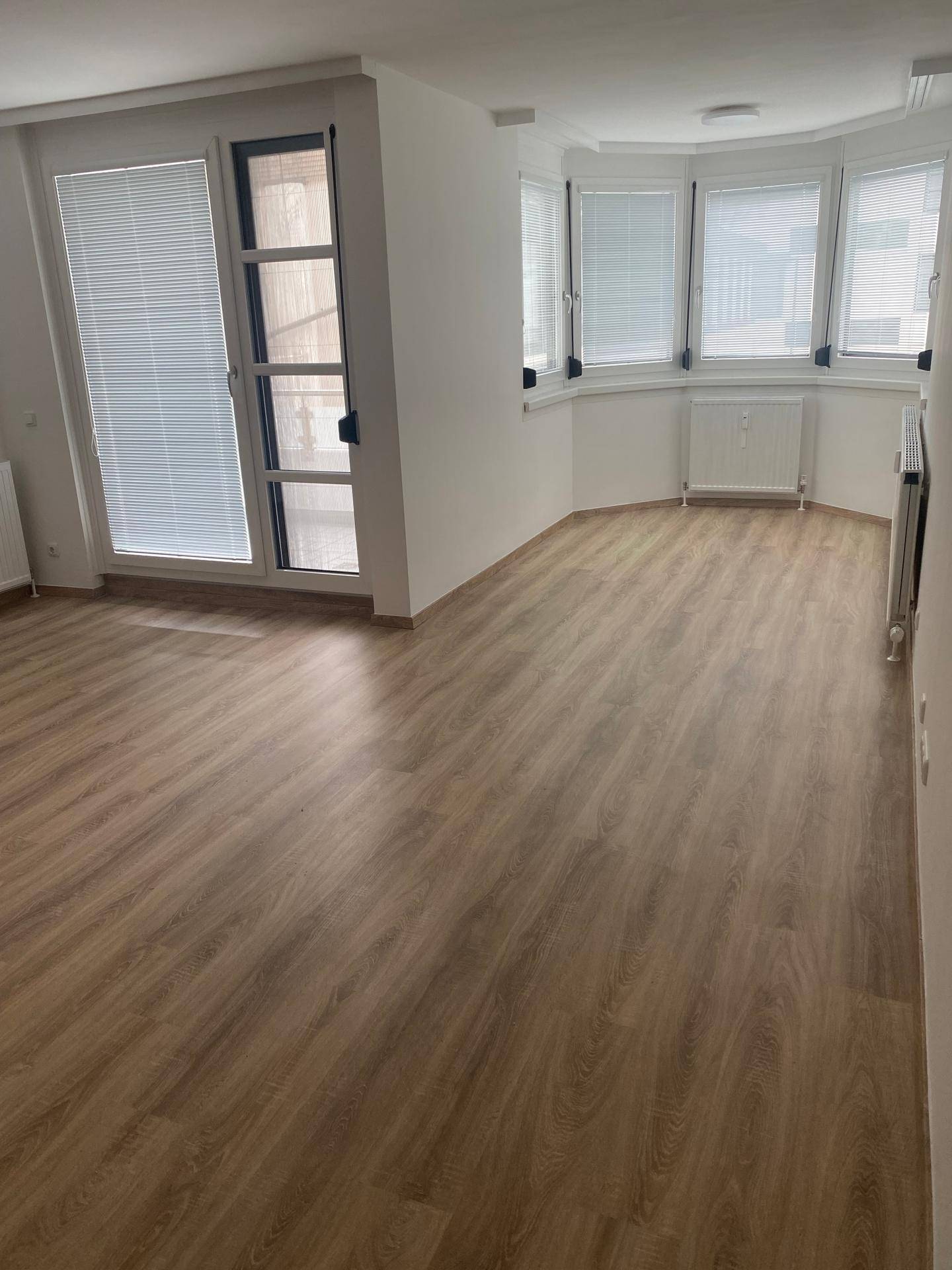Lichtdurchflutetes Wohnzimmer mit Laminatboden, Erkerfenstern und direktem Balkonzugang.