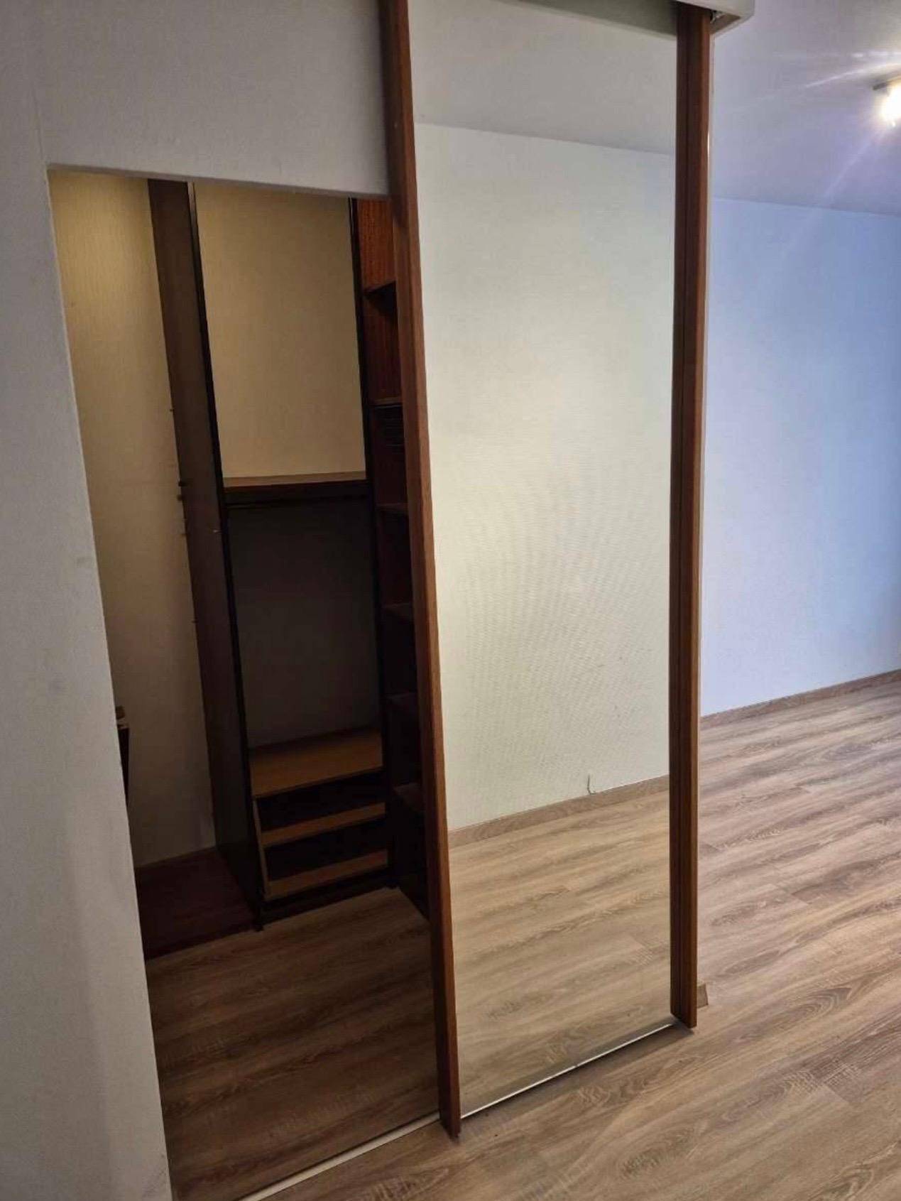 Raum mit Laminatboden und einer Spiegelschiebetür, die einen Einbauschrank offenbart.