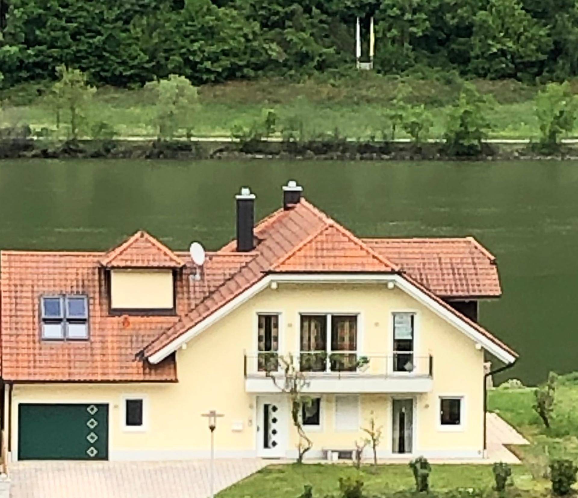 Hausansicht von oben mit rotem Ziegeldach, Balkon und weitem Blick auf den See.
