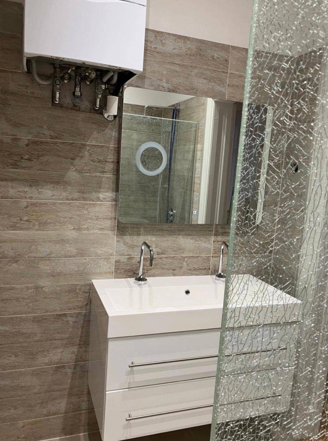Modernes Badezimmer mit Einzelwaschbecken, Spiegel und Duschbereich mit gemusterter Glaswand.