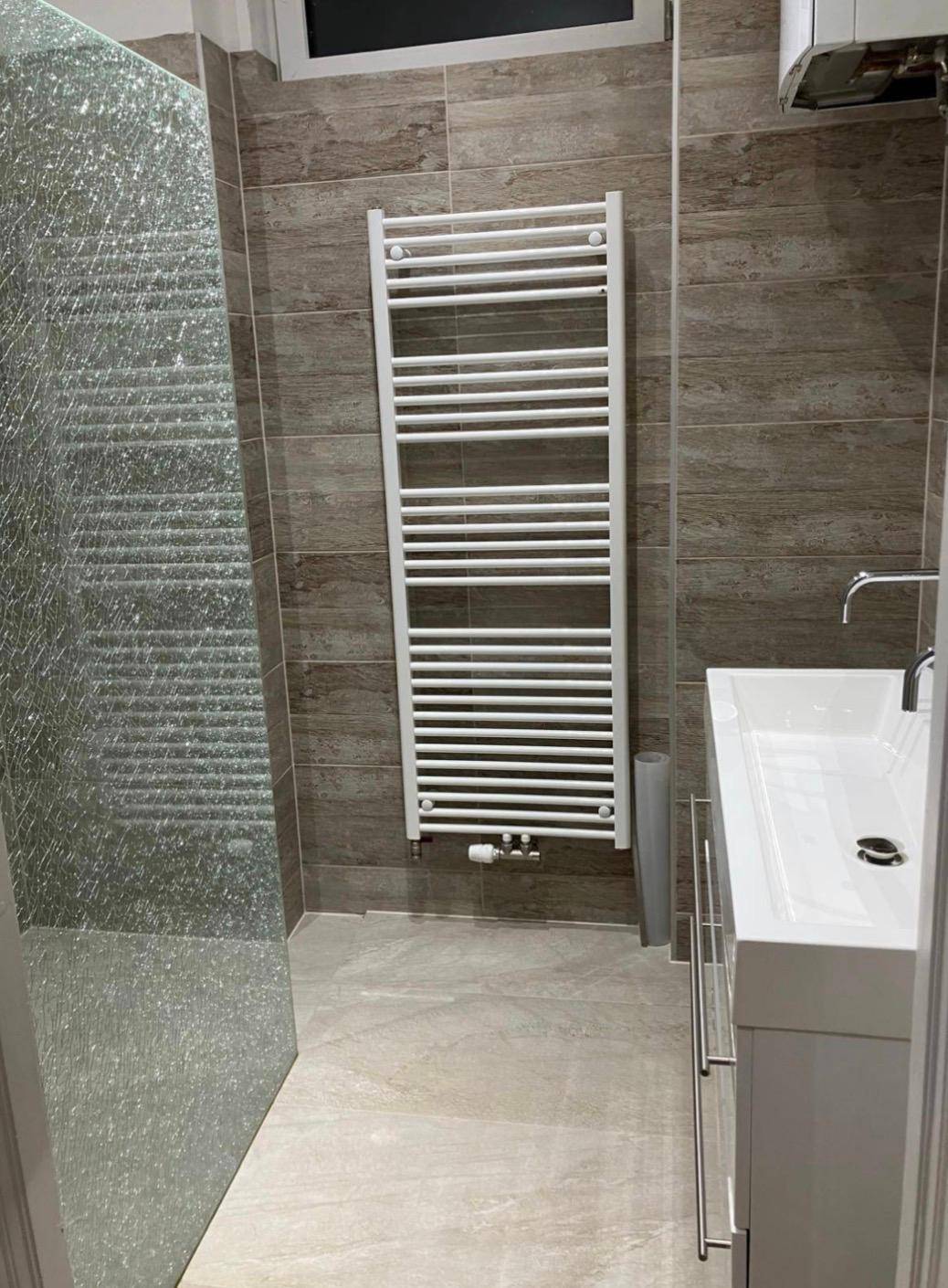 Badezimmer mit Duschbereich, Einzelwaschbecken und beheiztem Handtuchhalter an der Wand.