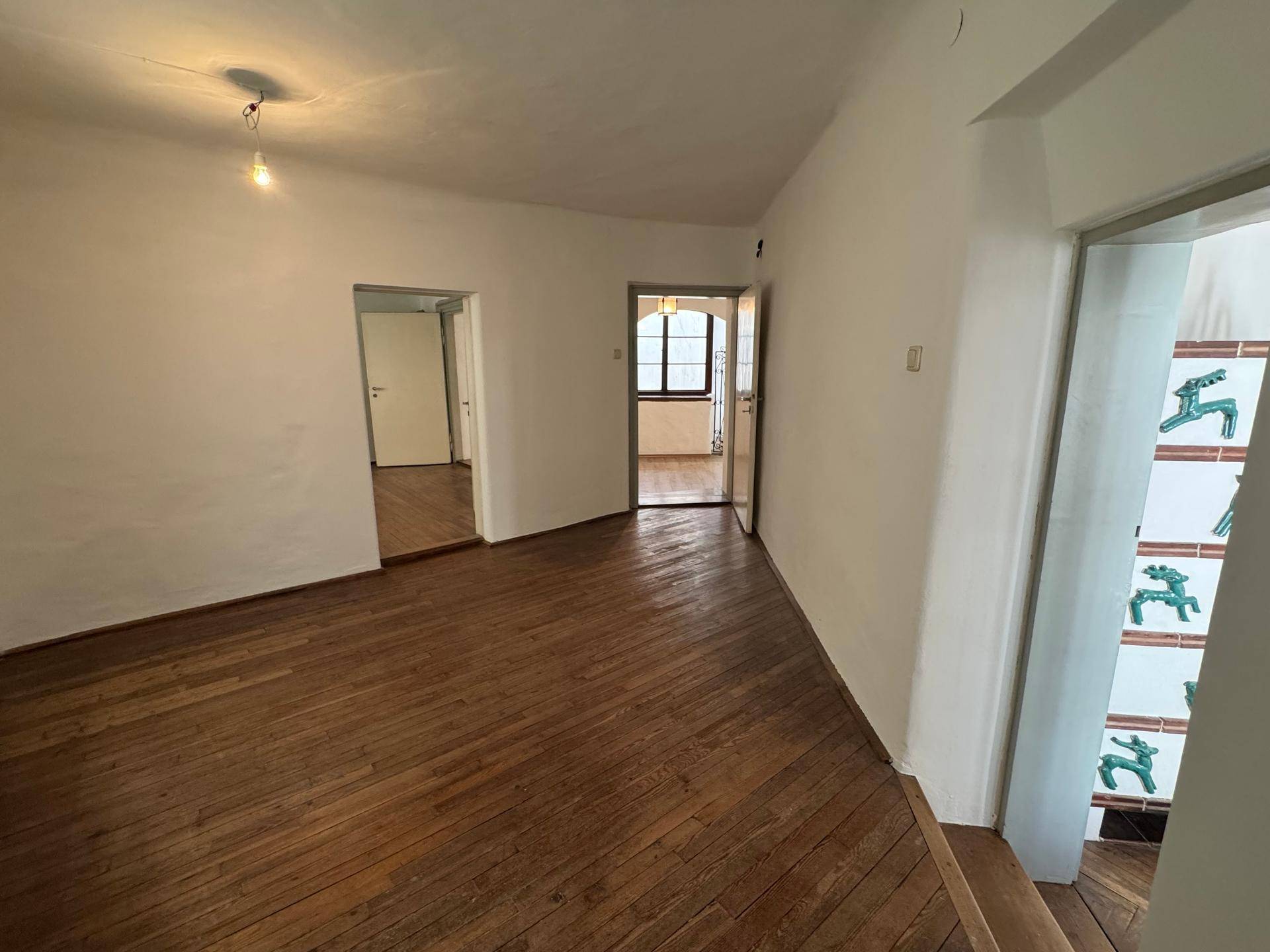 Helles Zimmer mit Holzboden und Zugang zu mehreren weiteren Räumen.