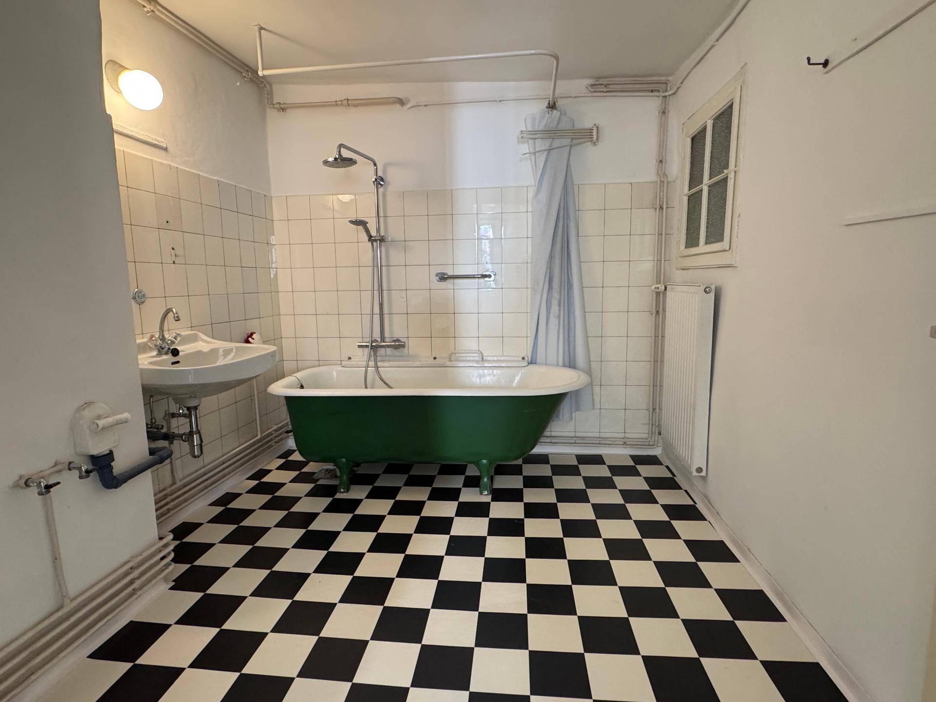 Badezimmer mit freistehender grüner Badewanne, Schachbrettmuster-Fliesen und Duschvorhang.