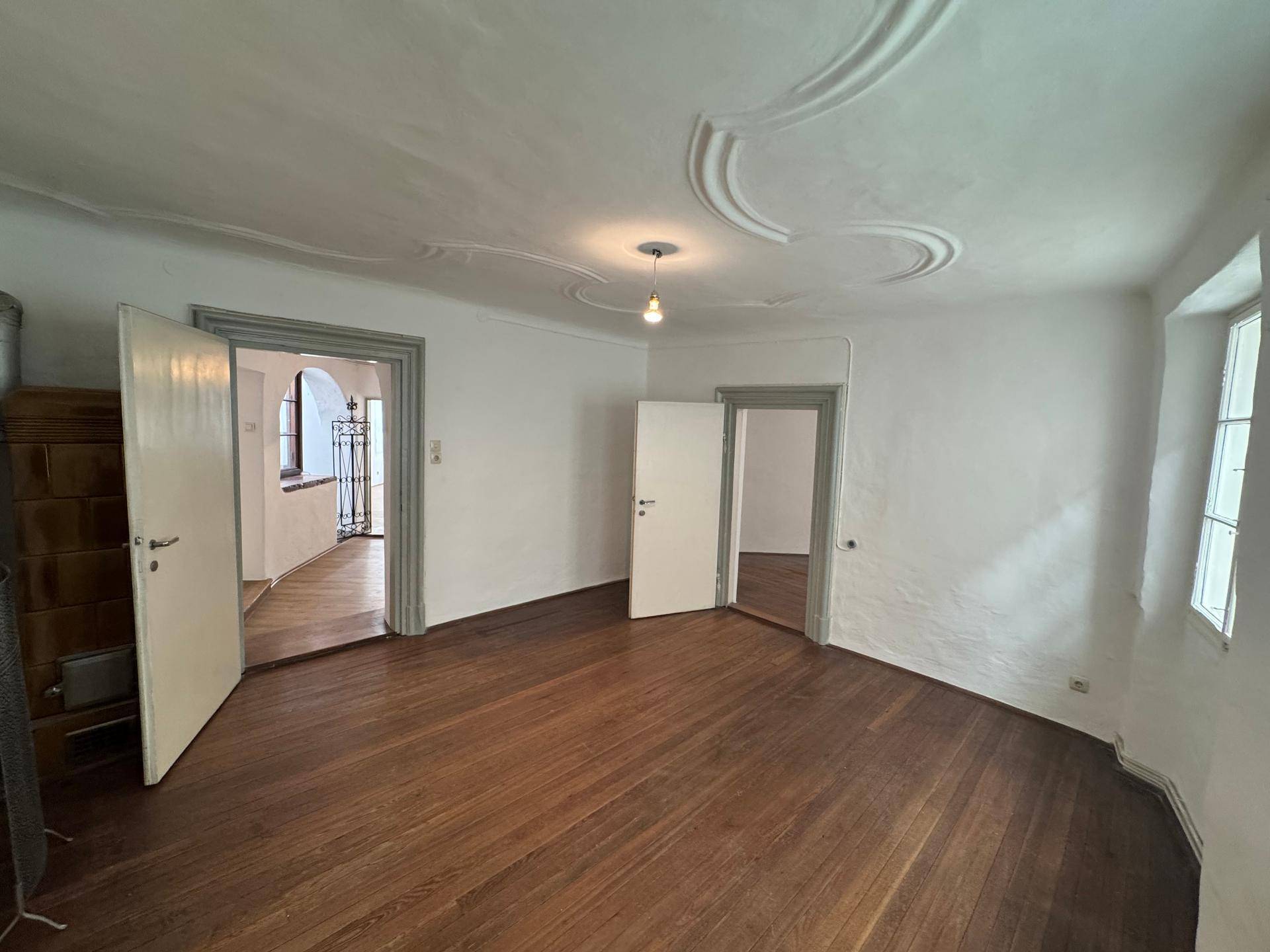 Geräumiges Zimmer mit Holzboden, Stuckdecke und mehreren Türen zu angrenzenden Räumen.